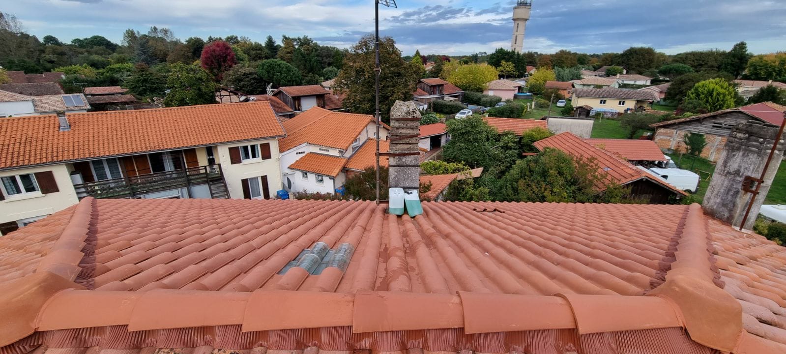 Toiture en tuiles rouges terminée avec faîtage et solin de cheminée neufs, vue panoramique sur le village